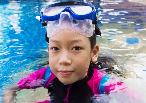 Girl relaxing on the side of a swimming pool wearing goggles and snorkel