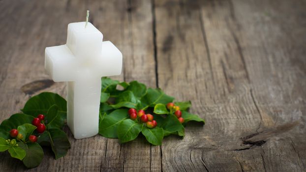 White Religious Candle surrounded by green leaves on wood background