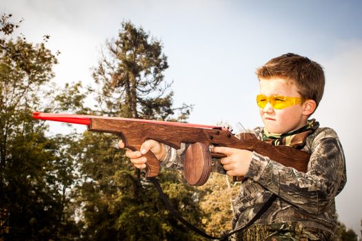 Young boy target shooting with toy rubber band gun in the park.