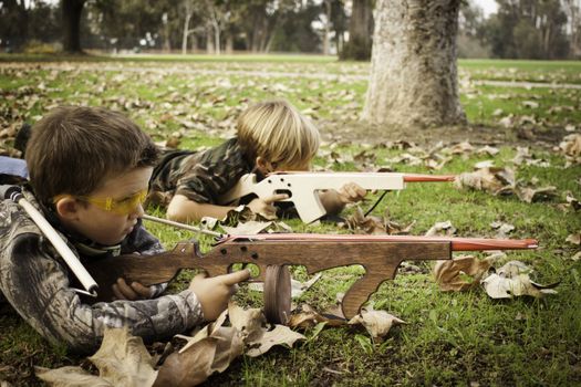 Young boys target shooting with toy rubber band gun in the grass at the park.