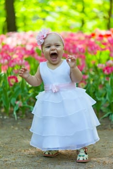 Baby in an elegant dress near blossoming tulips