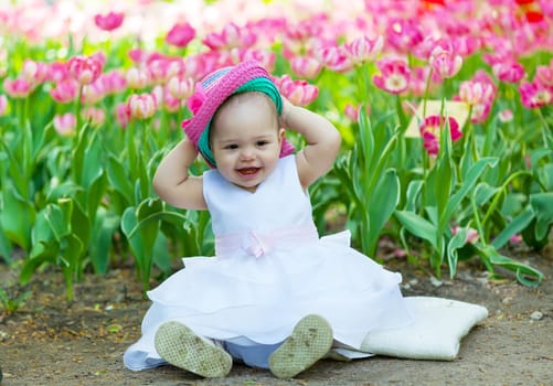Baby in an elegant dress near blossoming tulips