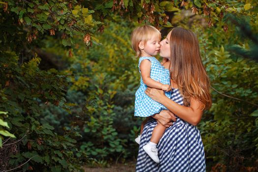 Mother holds daughter in his arms and kisses her on the cheek