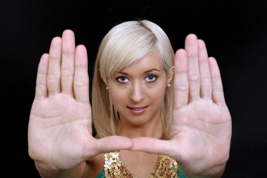 A lovely young blonde puts her hands to the camera, palm flat,framing her face.  Selective focus on her face.