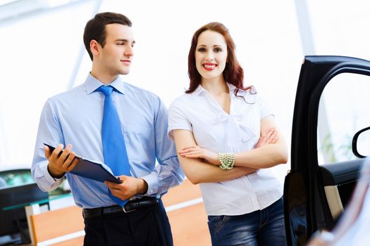 Attractive woman at car salon with consultant choosing a car