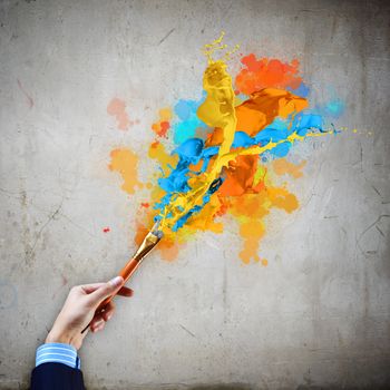 Close-up of human hand holding paint brush making colorful paint splashes