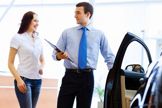 Attractive woman at car salon with consultant choosing a car