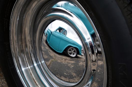 A hotrod being reflected in the hubcap of another custom car.