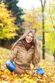 Young woman in a park, surrounded by autumn leaves falling