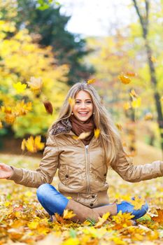 Young woman surrounded by autumn leaves falling