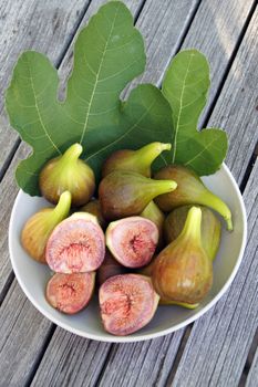 fresh figs in a white bowl with fig leafs on a wooden table