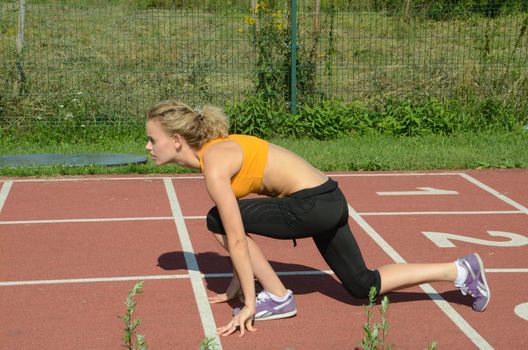Active young female starts run on the track. Blond girl wearing sport's outfit.