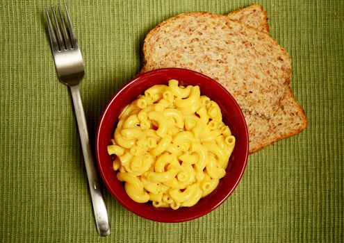 macaroni and cheese in red bowl served with bread on green background