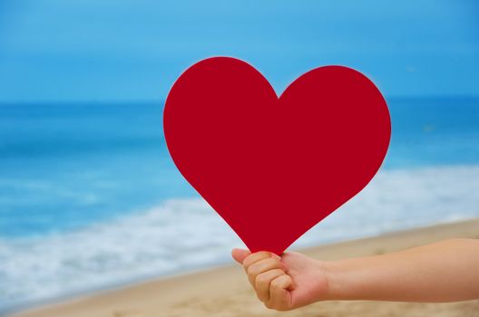 Girl holding heart shape on the beach - holiday concept