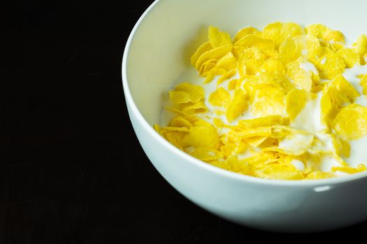 cornflakes in bowl on black table with milk in morning