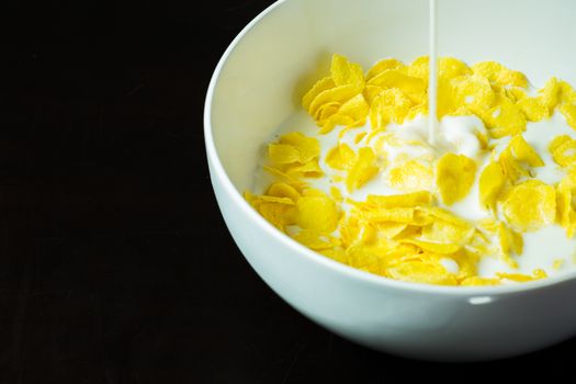 cornflakes in bowl on black table with milk in morning