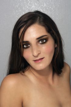 A close-up of a lovely young brunette with a textured grey background.