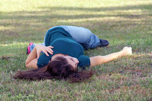 An attractive young brunette in casual wear relaxes outdoors, lying in the grass.