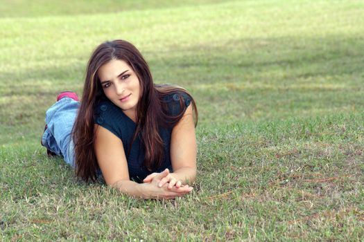 An attractive young brunette in casual wear relaxes outdoors, lying in the grass.