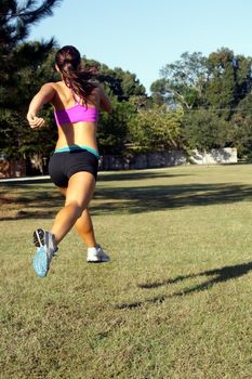 A lovely young athlete jogs away from the camera outdoors.  Generous copyspace.