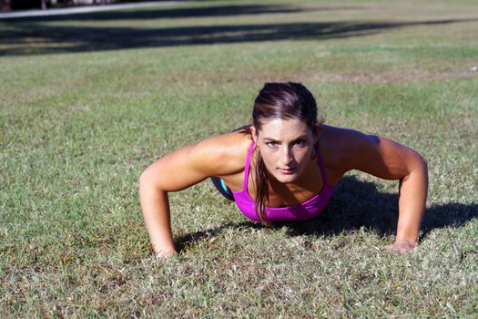 A lovely young athlete does pushups outdoors.  Generous copyspace.