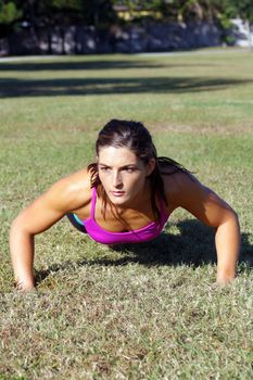 A lovely young athlete does pushups outdoors.  Generous copyspace.