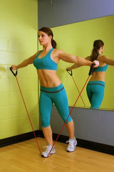 A lovely young brunette with exceptional muscle tone works out with resistance bands in front of a mirror.