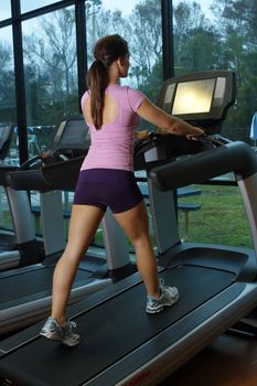 A lovely young, athletic brunette exercises on a treadmill.