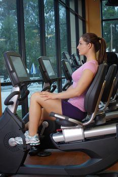 A lovely young, athletic brunette exercises on a cycling machine.