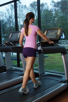 A lovely young, athletic brunette exercises on a treadmill.