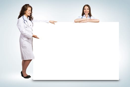 Two young woman doctor holding a blank banner, place for text