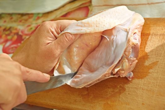 Bird meat cutting with a knife on a wooden kitchen board