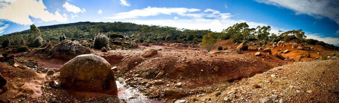 Panoramic view of an Australian desert landscape with rich brown earth and rocks stretching towards distant vegetation on the horizon