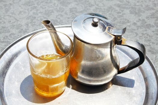 A kettle with a tea glass on a tray
