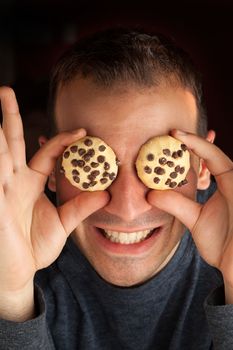 Crazy man holds cookies over his eyes.