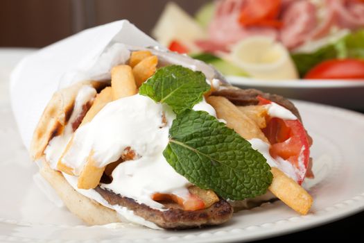 Traditional Gyro sandwich with meat  tzatziki sauce tomato onions and fried potato garnished with mint. Shallow depth of field.