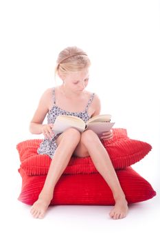 girl reads a book on red cushions against white background