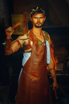 Hephaestus blacksmith in a leather apron in a forgery with a hammer on the shoulder