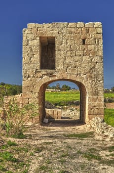 An elevated birthing chamber in the Maltese countryside, with an underlying arched underpass.