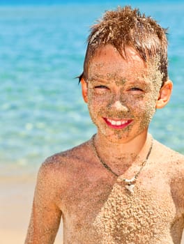 Happy boy covered with sand on a beach