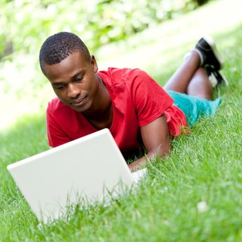 young smiling african student sitting in grass with notebook outdoor in summer man