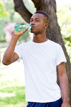athletic african young man drinking water outdoor in summer after fitness jogging sport
