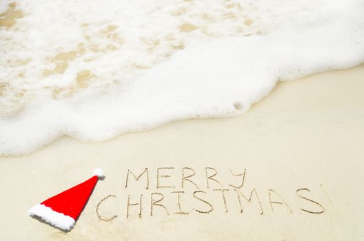 Sign "Marry Christmas" with christmas hat on the sandy beach - holiday concept