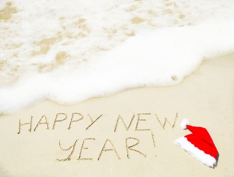 Sign "Happy 2014" with christmas hat on the sandy beach - holiday concept