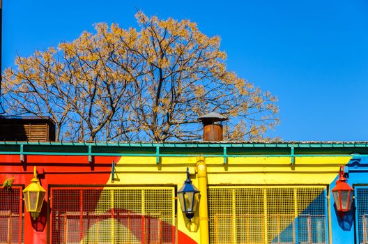 A red, yellow, and blue painted building with three lights and a beautiful blue sky in La Boca neighborhood of Buenos Aires