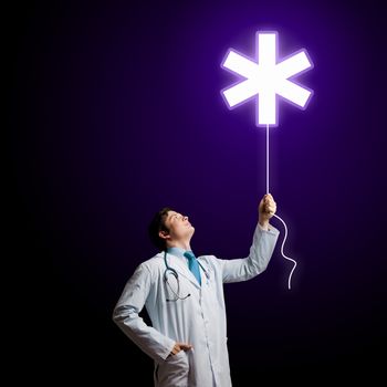 Young male doctor holding balloon with medical sign