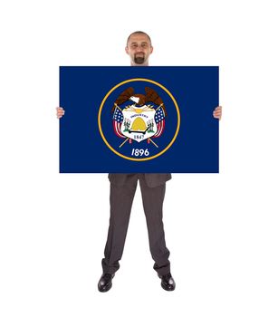 Smiling businessman holding a big card, flag of Utah, isolated on white