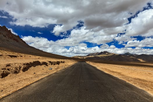 Travel forward concept background - road on plains in Himalayas with mountains and dramatic clouds. Manali-Leh road, Ladakh, Jammu and Kashmir, India