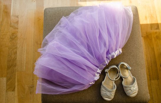 girls blown lilac ballerina skirt and light gray shiny shoes lying on the settee