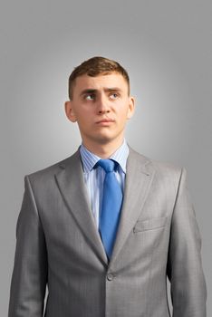 portrait of a young businessman thinking and looking up on gray background